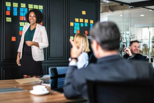 Smiling Woman in Blazer and Skirt Presenting to Colleagues 1